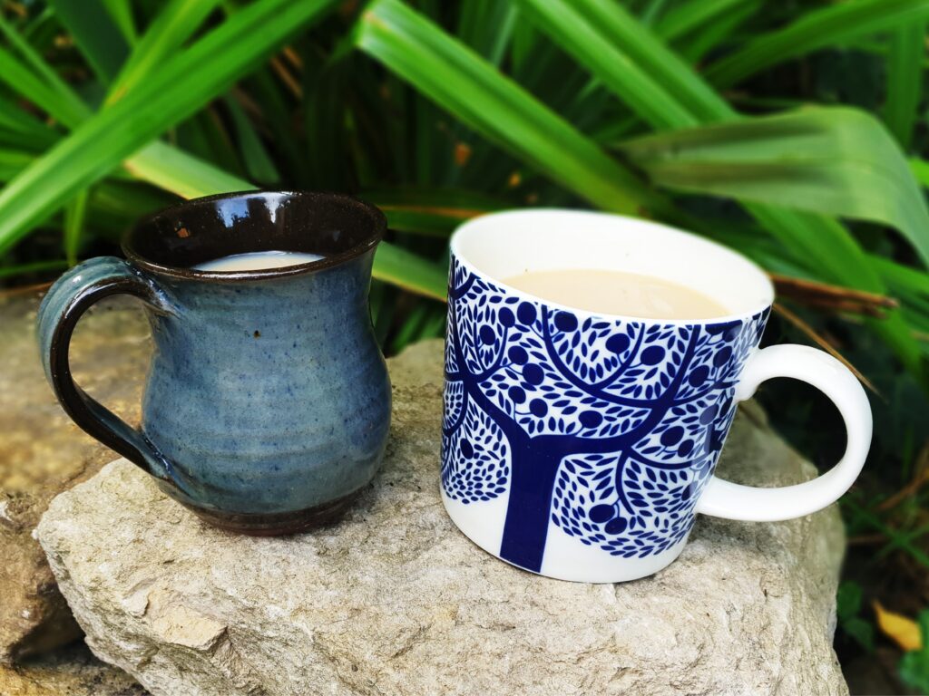 Close-up photo of two mugs of tea placed on a limestone wall, with greenery behind