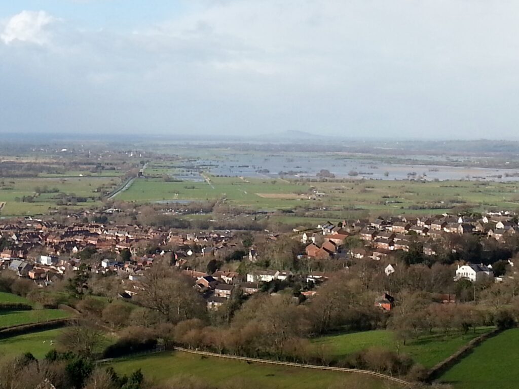 Landscape photo taken from Glastonbury Tor of an area of low-lying fields in flood in the distance, with part of the town in front