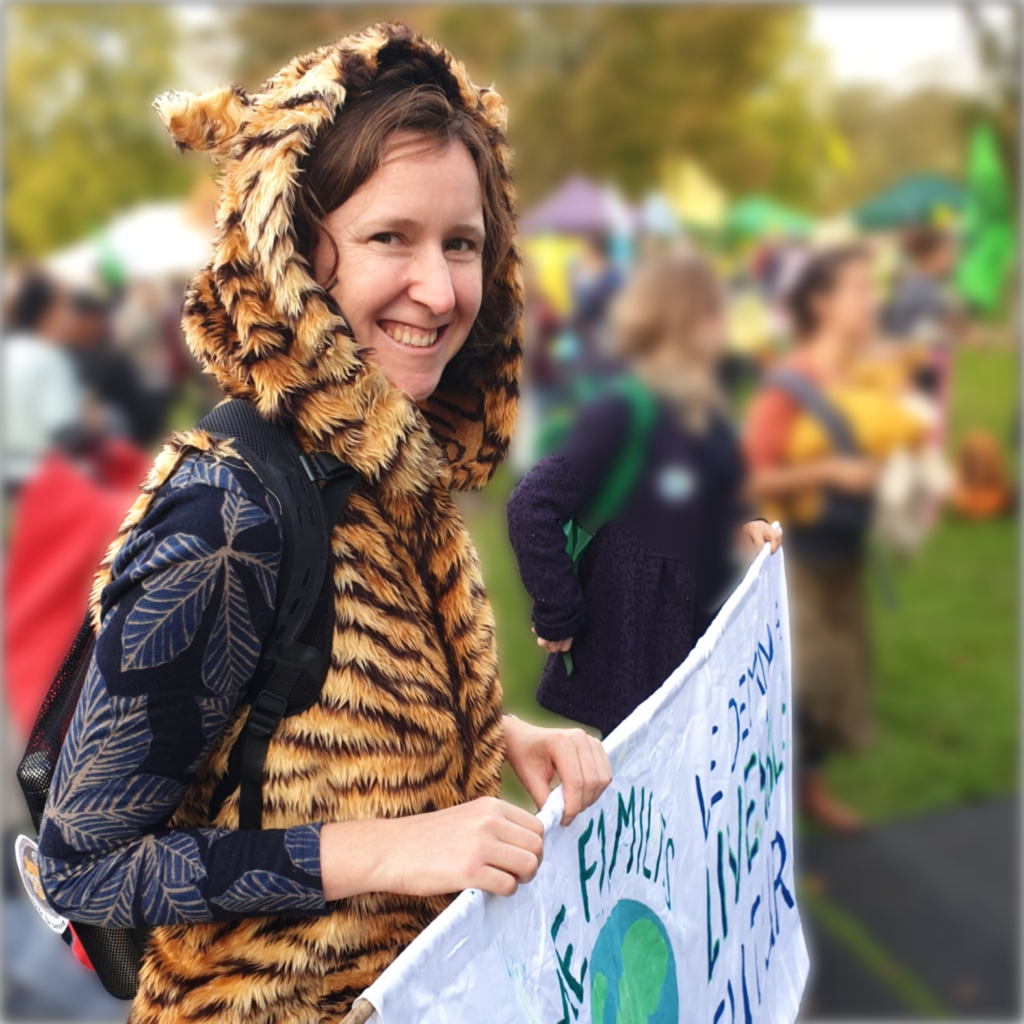 Photo of Ruth Gerrard at a nature and climate rally dressed in a tiger costume and holding a banner